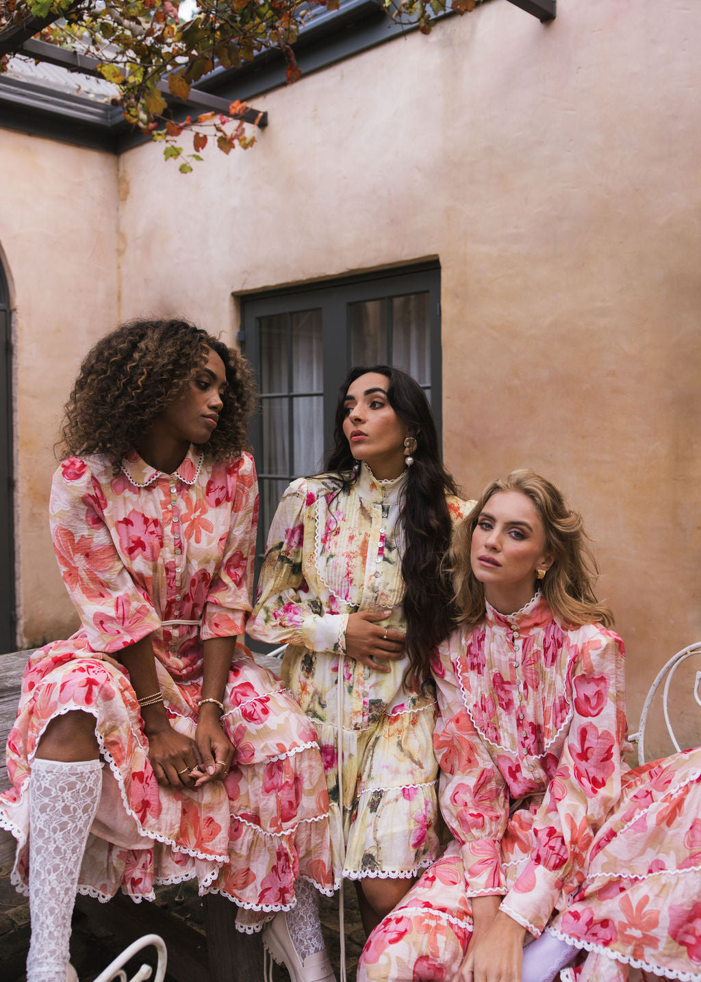 Tuscan Bloom campaign image by Analia the label of 3 beautiful women wearing romantic dresses with flowing gathered lace detailed tiers, long blouson sleeves in a viscose print of cream, peach, pink, yellow, ruby and olive blooms.